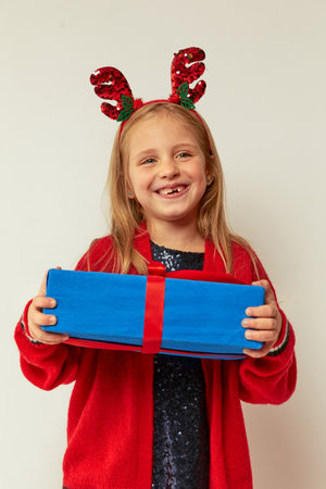 Smiling funny child (kid, girl) in Reindeer Hairband holding Christmas gifts in hand. christmas concept. Shooting on white backgroundの写真素材