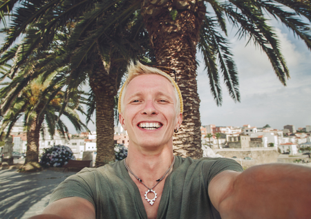 Young tanned guy shoots self-portrait in a background of palm treesの写真素材