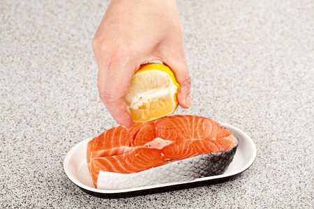 chief-cook squeezing lemon juice on a piece of fresh salmonの写真素材