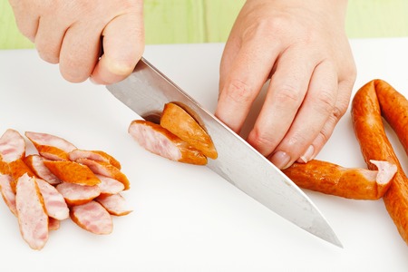 the process of cutting smoked sausage on a cutting board closeupの写真素材