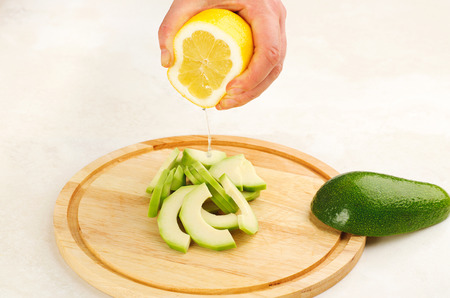 add lemon juice to sliced avocado on a cutting board closeup