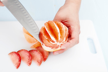 cook cleans and cuts grapefruit on a cutting board closeupの写真素材