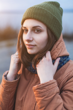 Young attractive girl in a green hat and jacket near the river in the sunset light. Close-up woman's portrait outdoors. Lifestyle. Soft focusの写真素材