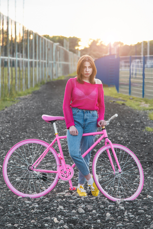 Sexy girl standing next to a trendy bike outdoors during sunset. Soft lightの写真素材