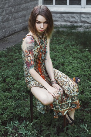 Attractive young girl in a dress sitting in the garden and sad. Portrait of fashionable girl hipster in the shady gardenの写真素材