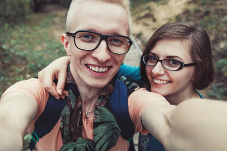 Young cheerful couple in glasses makes selfe outdoors and smiling. Beautiful young couple smiling at the cameraの写真素材