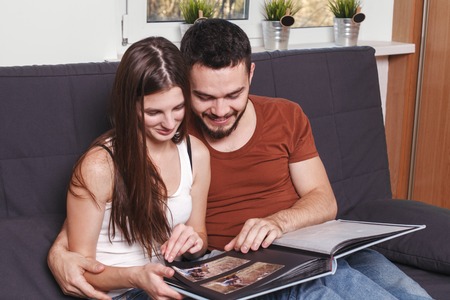 Young couple Leafs family album at home.Beautiful couple sitting on sofa at home and flips through the album.の写真素材