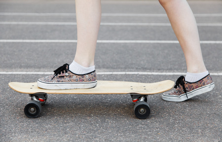 Young girl learning to ride a longboard. Close-up of legs