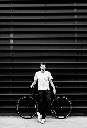 Hipster young man in a white T-shirt with a bicycle. Male citizen with fixed gear bike in an urban environmentの写真素材