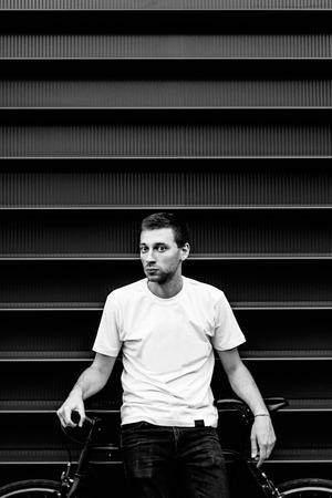 Close up portrait of hipster young man in a white T-shirt with a bicycle. Male citizen with fixed gear bike in an urban environmentの写真素材