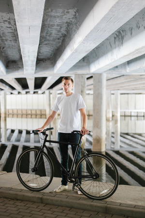 Young attractive man with a fashionable bicycle under a bridgeの写真素材