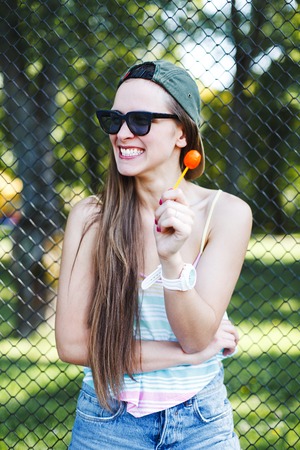 Young happy hipster girl in sunglasses and a cap with lollipopの写真素材