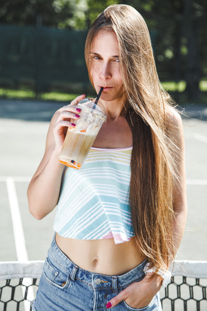 Beautiful hipster girl with long dark hair drinking a milk shake outsideの写真素材