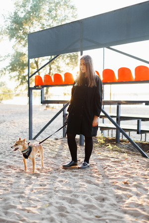 Beautiful young girl walking with a japanese dog on the beach on a sunny day in autumnの写真素材