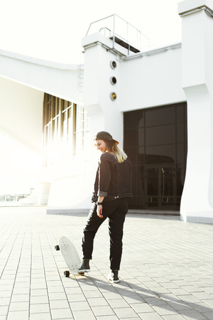 Young hipster brunette girl stands on longboard near modern architecture buildingの写真素材
