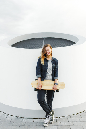 Smiling hipster girl with longboard in her hands in urban environmentの写真素材