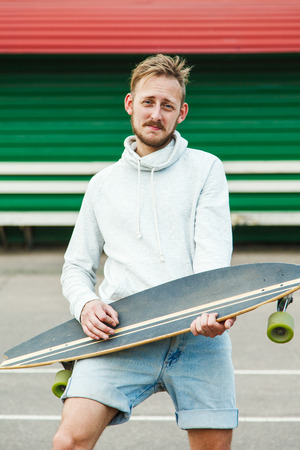 Cheerful hipster man fooling around with a longboard at the stadiumの写真素材