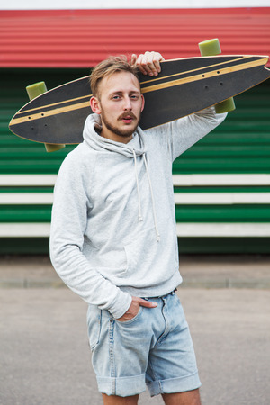 Sexy hipster man standing with longboard on his shoulderの写真素材