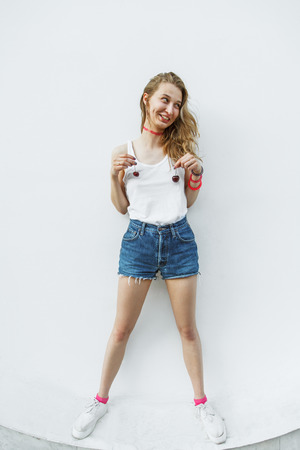 Young pretty hipster girl having fun with cherries near the white wallの写真素材