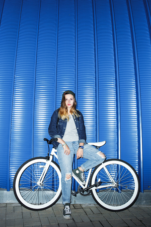 Fashionable girl posing with beautiful bicycle near the wallの写真素材