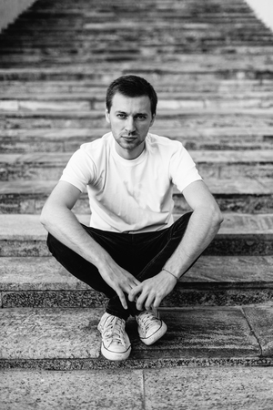 Portrait of sad young man sitting on the steps. Black and white portrait of a manの写真素材