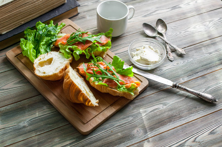 The fresh baked croissants with butter, a salty salmon and leaves of arugula on a chopping board on a wooden table. Breakfast conceptの写真素材