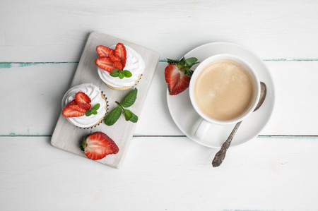 Vanilla cupcakes with butter cream and fresh strawberry and a cup of coffee on a light wooden background. Top viewの写真素材