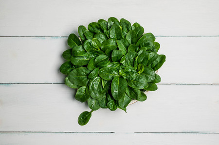 Spinach leaves on a plate on a wooden light background. Organic healthy food. Top viewの写真素材