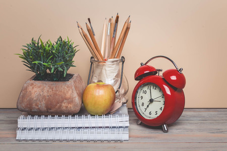 Writing-books, alarm clock, pencils, apple on a wooden background. Back to school concept