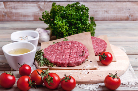 Cutlets for burgers from fresh minced meat with spices, herbs, Cherry tomatoes on a wooden table.の写真素材