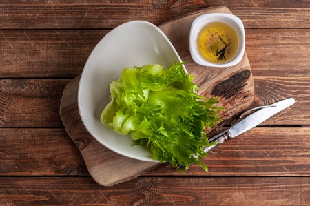 Fresh green lettuce in a plate and olive oil with spices on a wooden background. Top viewの写真素材