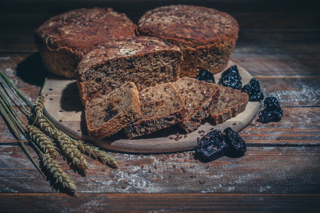 Rye bread with flax seeds and prunes on a wooden background. Homemade baking. Low key lighting. Light toningの写真素材
