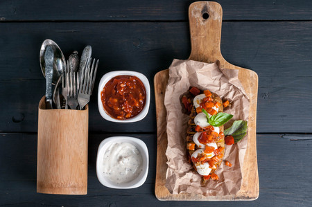 Baked potatoes with mozzarella cheese, vegetables and spices on a wooden background. Vegetarian...