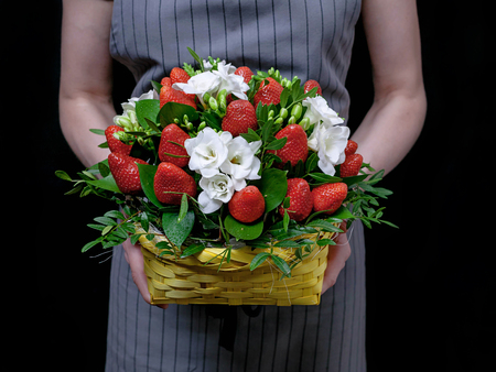 The florist holds a basket with flowers and strawberries on a dark background. Florist at workの写真素材