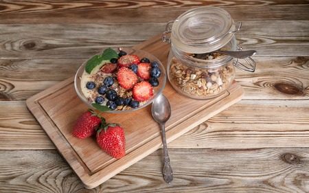 Granola with nuts, yogurt, fresh blueberries and strawberries in a glass bowl on a wooden backgroundの写真素材