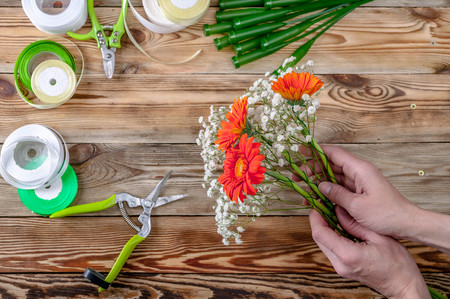 The florist's hands make a bouquet of flowers. People behind the work concept Top viewの写真素材