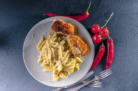Penne pasta with pesto sauce and fried cutlets and turkey, hot chili and cherry tomatoesの写真素材