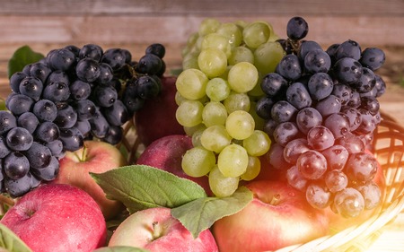 Ripe red apples with leaves, black and white grapes in a basket. Autumn harvest. Close-up.