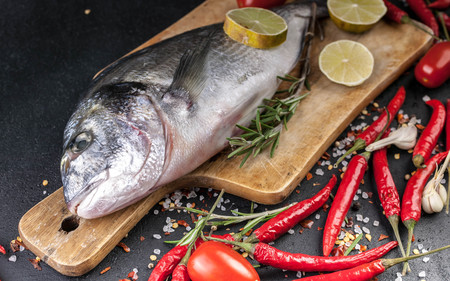 Fresh Dorado on a wooden cutting board. Aromatic herbs, lime, cherry tomatoes, salt, paprika and...
