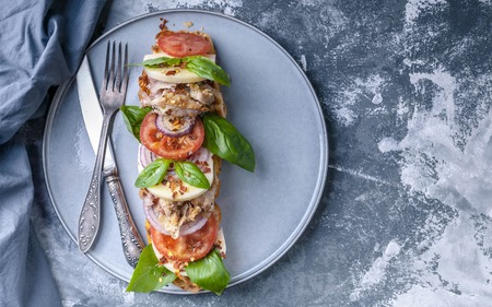 Delicious Italian sandwich with smoked chicken, mozzarella, tomatoes, sweet onions and basil leaves on a round plate on a concrete background. Top viewの写真素材