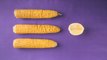 Boiled corn and lemon on a purple background. Top view