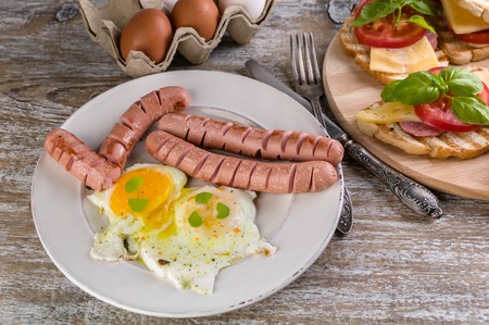 Fried eggs, sausages, sandwiches with cheese, tomato and basilの写真素材