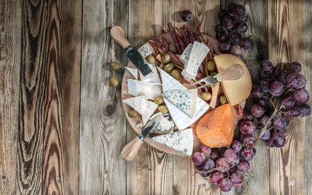 Different sorts of cheese and grapes on a wooden background. Top view
