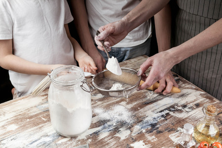 Mom with children sift flour for dough. Hands of mother and her children. Cooking with kids....