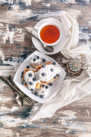 Viennese waffles with cream and blueberry, tea in a white cup. Top viewの写真素材