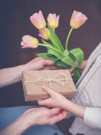 The girl congratulates her mother and gives a gift and tulips. Happy Mother's Day concept. Toning. Vertical shot Selective focusの写真素材