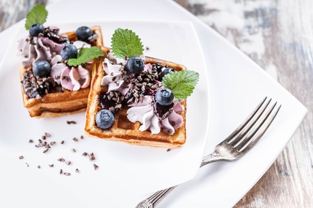 Belgian waffles with cream, jam, blueberries and mint leaves on a white plate. Close-up. Delicious Dessertの写真素材
