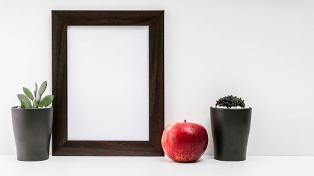 Empty dark photo frame, two succulents in dark pots and a red juicy apple on a white background. Scandinavian style in the interior.の写真素材