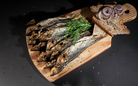 Hot smoked herring, red onion and dill, rye bread on a cutting board on a dark background.の写真素材