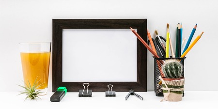 Banner mock-up of a dark photo frame, cactus, a glass of orange juice, color pencils and stationery on a light background.の写真素材